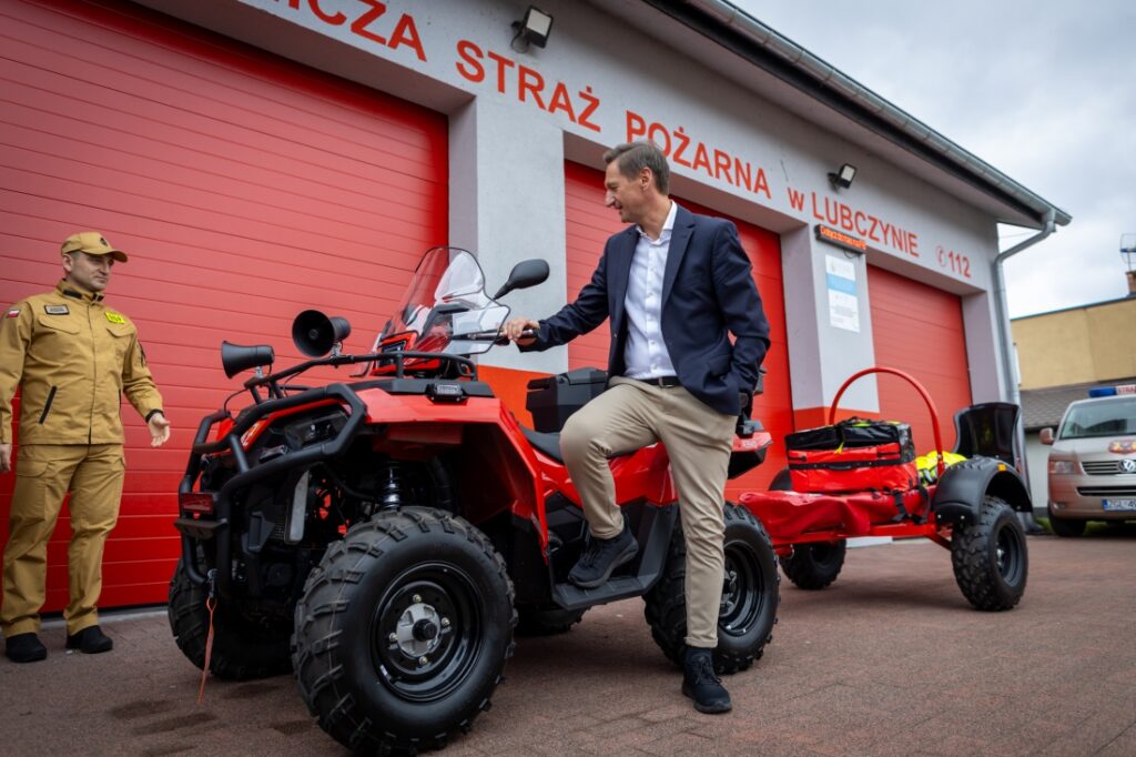 Marszałek Województwa Zachodniopomorskiego Olgierd Geblewicz stoi przy nowym quadzie przed remizą OSP Lubczyna. Obok niego stoi także strażak.