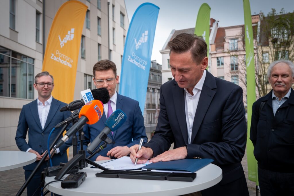 Marszałek Województwa Zachodniopomorskiego Olgierd Geblewicz, zastępca prezydenta Szczecina Michał Przepiera, w towarzystwie innych osób podczas podpisywania umowy o dofinansowanie przebudowy Placu Orła Białego w Szczecinie, 22.04.2025