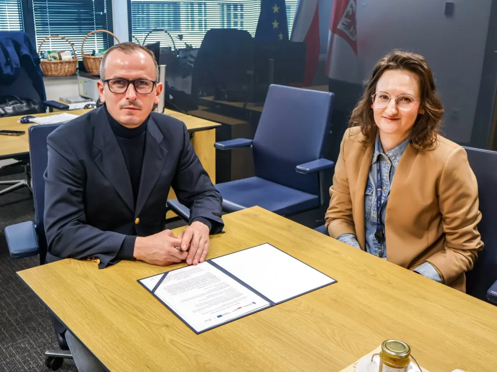 Członek Zarządu Województwa Marcin Łapeciński siedzi za stołem wraz z przedstawicielką rzeszowskiej firmy Geokart-International podczas podpisywania umowy na aktualizację baz danych obiektów topograficznych.